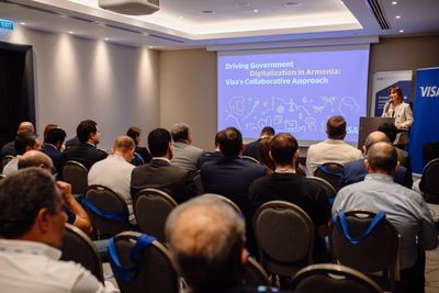 Կարճ շագանակագույն մազերով մի կին կանգնած է բեմում՝ ներկայացնելով թեման միջոցառման ժամանակ։Նա ներգրավված խոսում է հանդիսատեսի հետ։Նրա հետևում տեսանելի է ներկայացման տեսասահիկը: