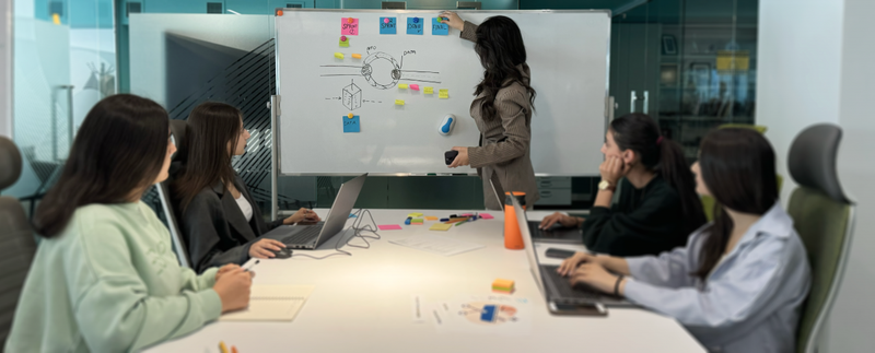 Մի խումբ երիտասարդներ սեղանի շուրջ համախմբված նայում են գրատախտակին